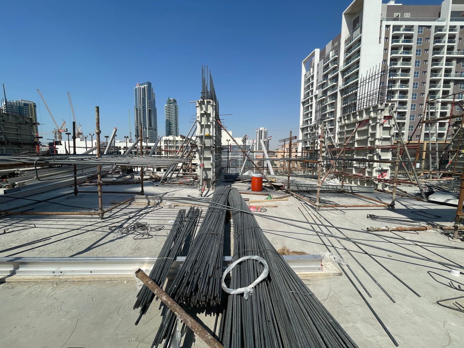 Pearl House By Imtiaz Construction site with steel rods and scaffolding, surrounded by buildings under clear blue skies.